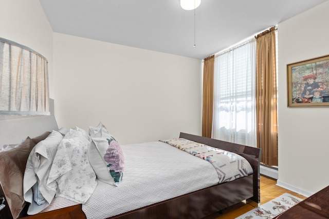 bedroom with light hardwood / wood-style floors and a baseboard heating unit