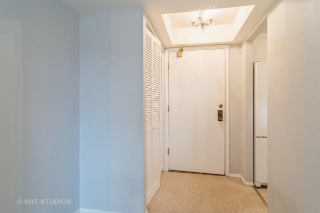 corridor featuring a chandelier, light colored carpet, and a raised ceiling