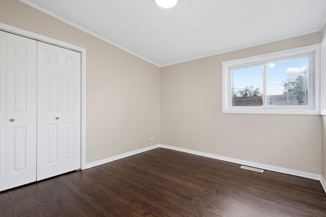 unfurnished bedroom with dark hardwood / wood-style floors, ornamental molding, and a closet