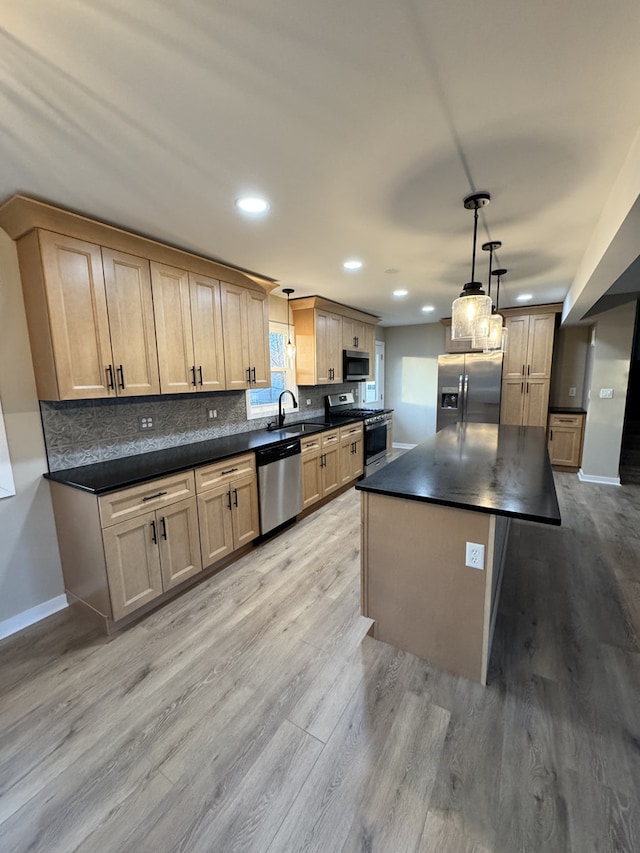 kitchen with appliances with stainless steel finishes, light brown cabinetry, sink, pendant lighting, and a kitchen island