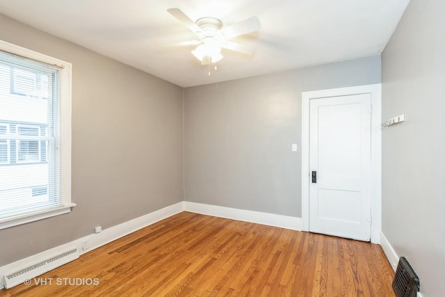 empty room featuring hardwood / wood-style flooring, ceiling fan, and a baseboard heating unit