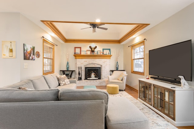 living room with light hardwood / wood-style floors, a tray ceiling, crown molding, a fireplace, and ceiling fan