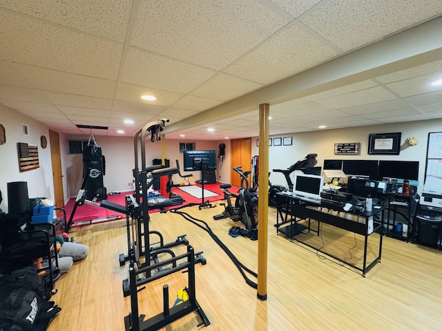 exercise room with a drop ceiling and light wood-type flooring