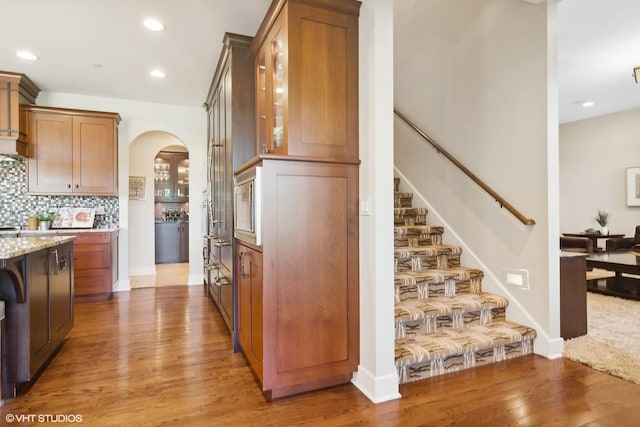 kitchen with decorative backsplash, light stone counters, wood-type flooring, and stainless steel microwave