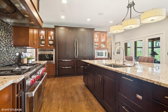 kitchen with sink, hanging light fixtures, wall chimney range hood, backsplash, and appliances with stainless steel finishes