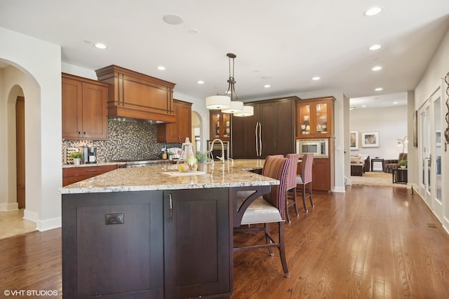 kitchen with a kitchen bar, dark wood-type flooring, pendant lighting, stainless steel microwave, and a large island