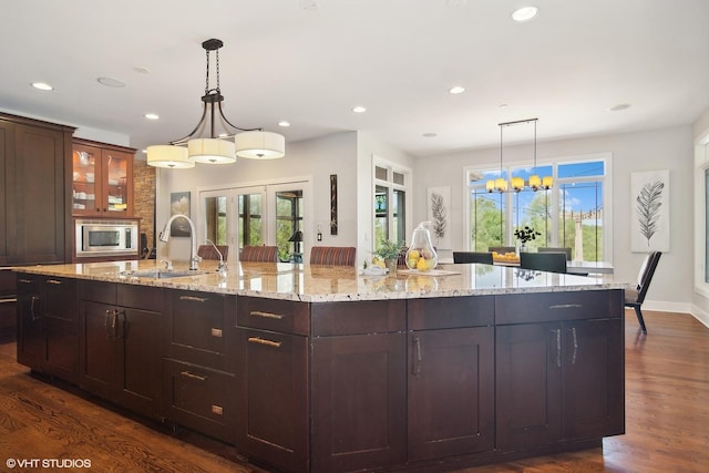 kitchen featuring decorative light fixtures, sink, dark wood-type flooring, and a large island with sink