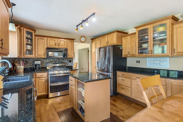 kitchen with sink, stainless steel appliances, dark stone counters, a kitchen island, and light wood-type flooring