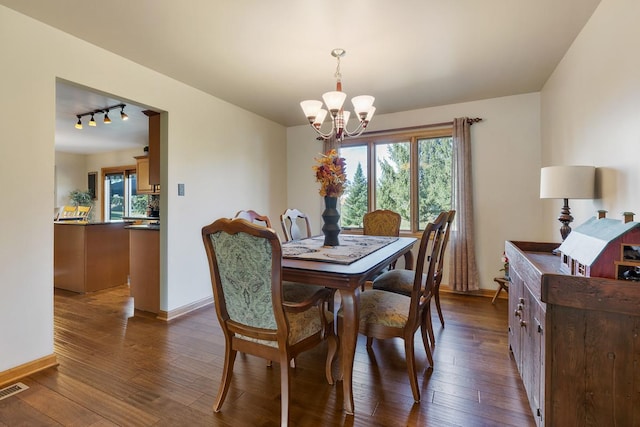 dining space featuring a chandelier, rail lighting, and dark wood-type flooring