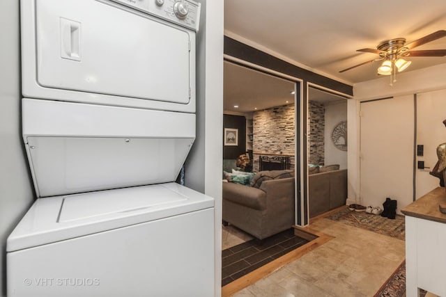 clothes washing area with stacked washer / dryer, ceiling fan, and a fireplace