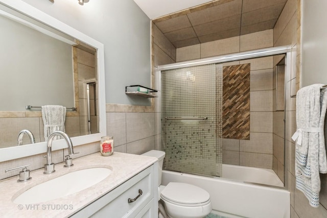 full bathroom with shower / bath combination with glass door, vanity, toilet, and tile walls