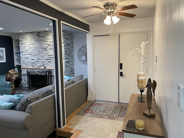 foyer entrance with ceiling fan, a fireplace, and ornamental molding