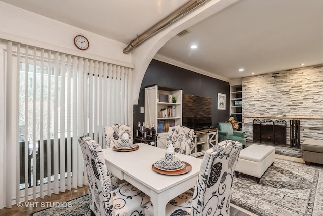 dining room with tile patterned floors, a stone fireplace, built in shelves, and ornamental molding