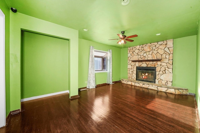 unfurnished living room featuring dark hardwood / wood-style floors, a stone fireplace, and ceiling fan