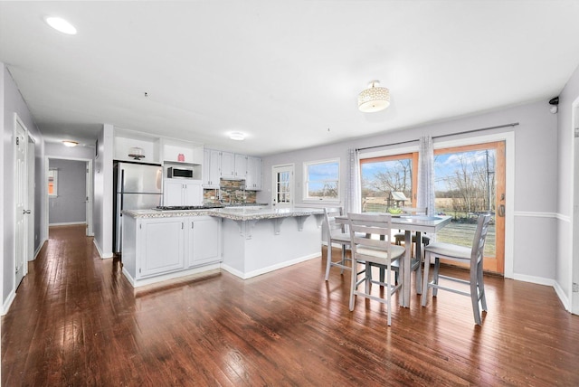 kitchen featuring white cabinetry, light stone countertops, stainless steel appliances, tasteful backsplash, and dark hardwood / wood-style floors