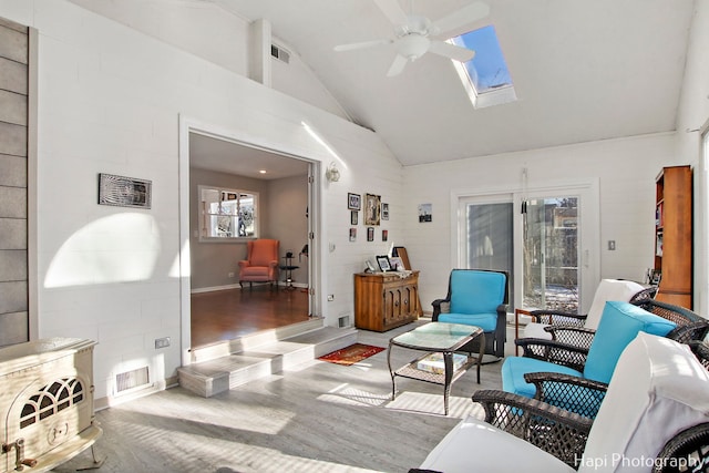 living room with hardwood / wood-style floors, ceiling fan, high vaulted ceiling, and a skylight