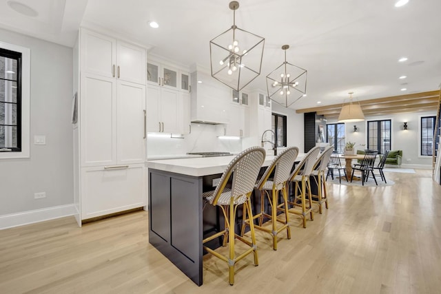 kitchen featuring a breakfast bar, decorative light fixtures, white cabinets, a large island, and light wood-type flooring