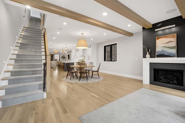 dining area featuring beamed ceiling, an inviting chandelier, a high end fireplace, and light hardwood / wood-style flooring