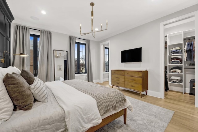 bedroom with an inviting chandelier, a walk in closet, light hardwood / wood-style floors, and a closet