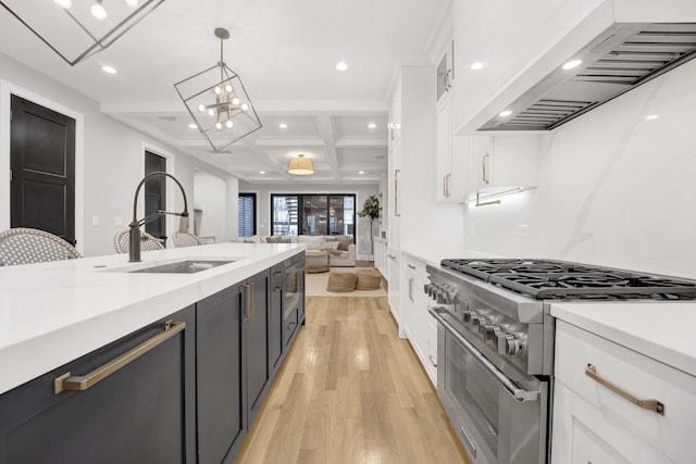 kitchen featuring pendant lighting, high end stove, sink, white cabinets, and wall chimney range hood