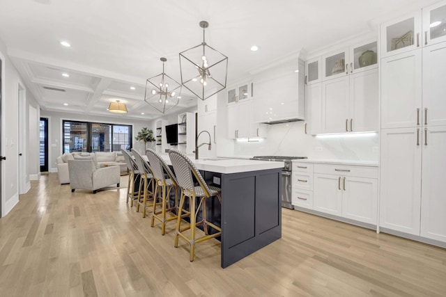 kitchen with high end range, hanging light fixtures, an island with sink, and white cabinets