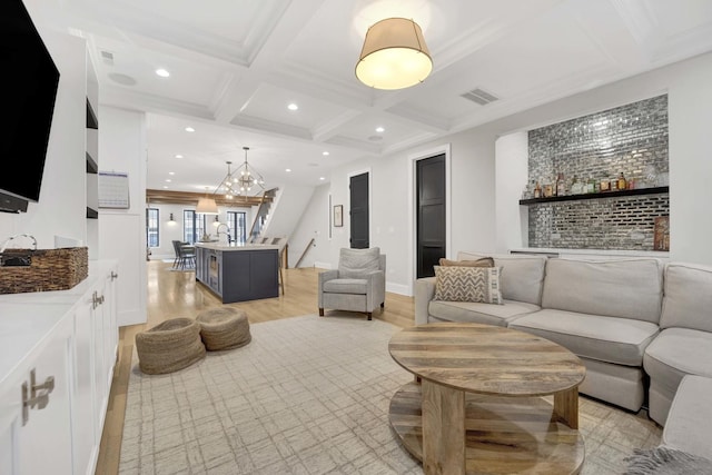 living room featuring light wood-type flooring, coffered ceiling, a notable chandelier, crown molding, and beam ceiling