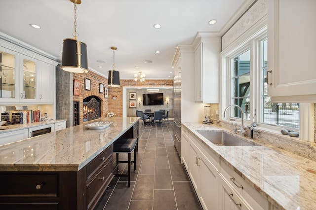 kitchen featuring glass insert cabinets, white cabinets, a sink, brick wall, and dark tile patterned floors