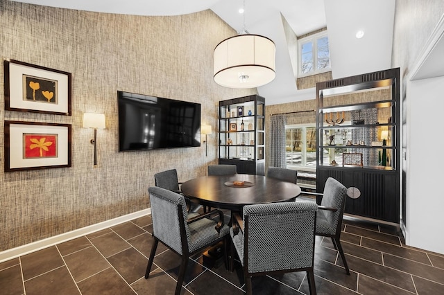 dining space with high vaulted ceiling, dark tile patterned flooring, baseboards, and wallpapered walls