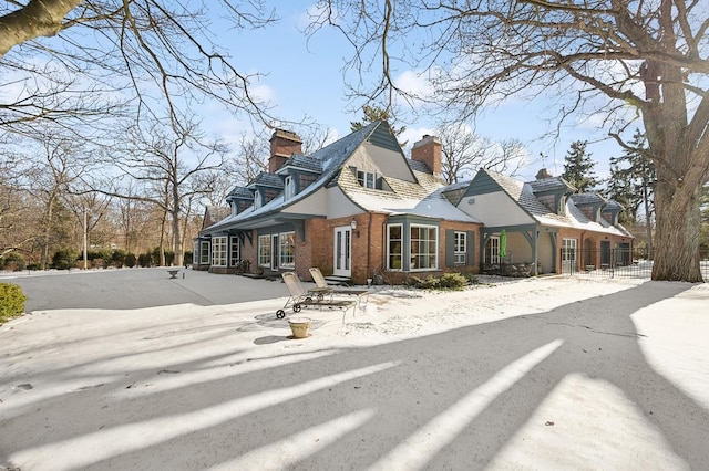 cape cod-style house featuring a chimney, fence, and brick siding