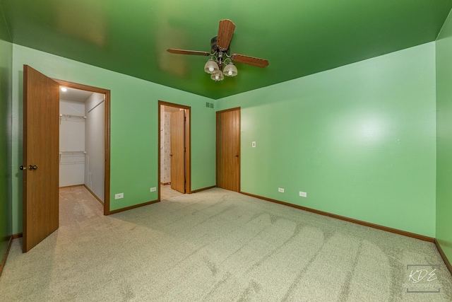 unfurnished bedroom featuring light carpet, ceiling fan, a walk in closet, and a closet