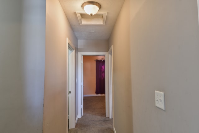 corridor featuring a textured ceiling, carpet floors, attic access, and baseboards