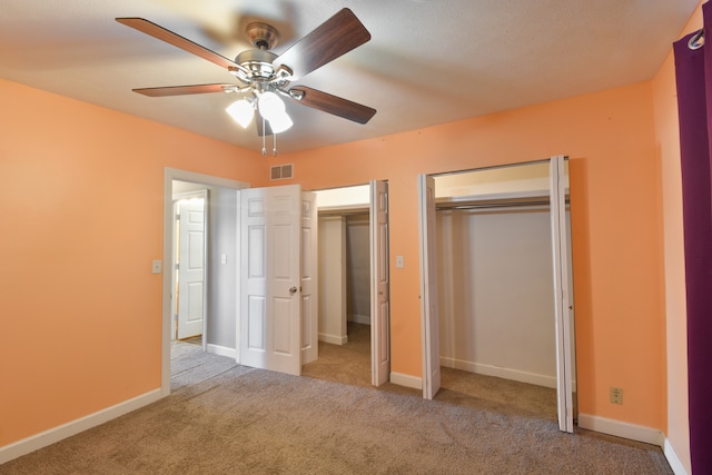 unfurnished bedroom with baseboards, visible vents, ceiling fan, carpet flooring, and multiple closets