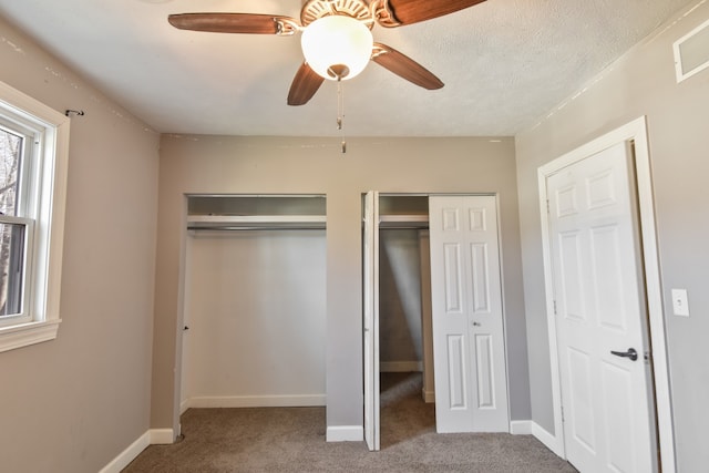 unfurnished bedroom featuring a textured ceiling, carpet flooring, visible vents, baseboards, and two closets