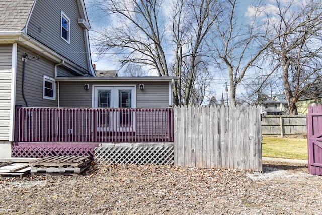 view of home's exterior featuring a deck, a shingled roof, and fence