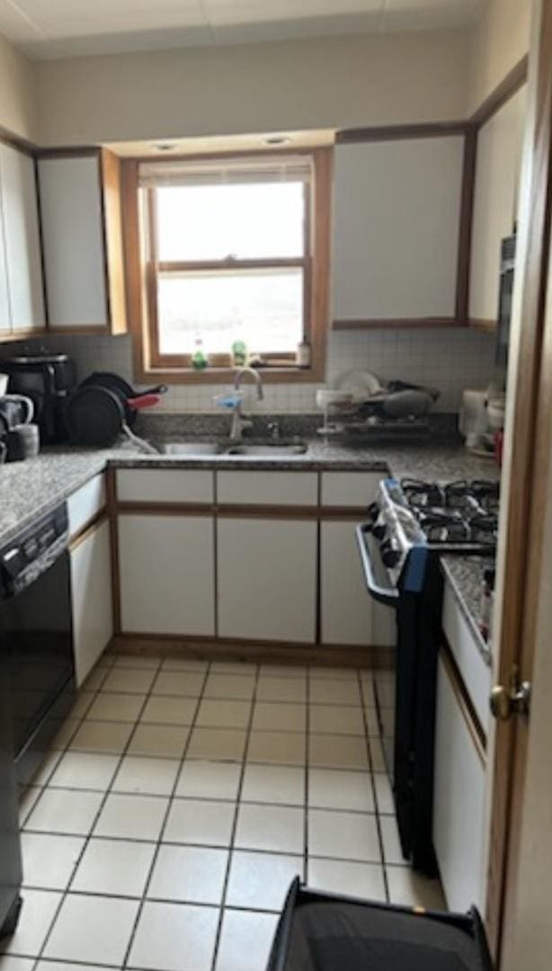 kitchen with stainless steel gas range, sink, light tile patterned floors, black dishwasher, and white cabinetry