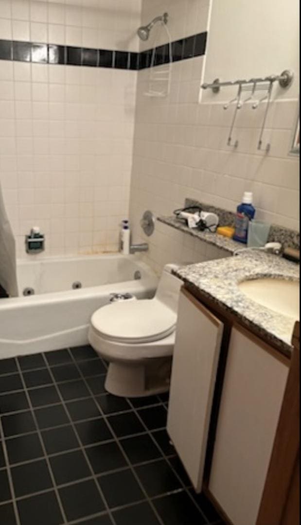 full bathroom with shower / bathtub combination with curtain, tile patterned flooring, toilet, vanity, and tile walls