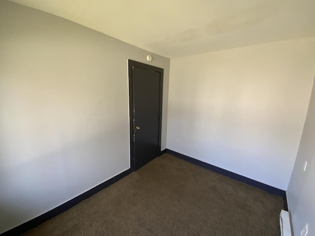 spare room featuring dark carpet and a baseboard heating unit