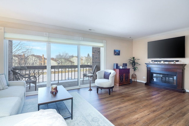 living room featuring crown molding, visible vents, a glass covered fireplace, wood finished floors, and baseboards