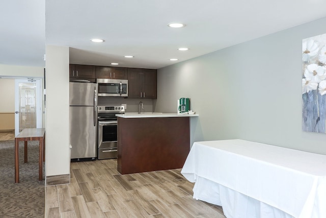 kitchen with light wood-type flooring, appliances with stainless steel finishes, dark brown cabinets, and sink