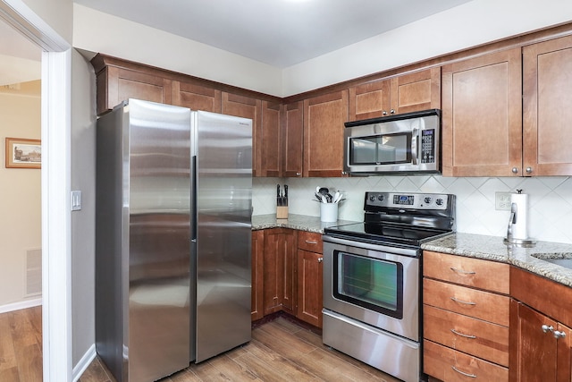 kitchen featuring backsplash, light stone countertops, stainless steel appliances, and hardwood / wood-style floors