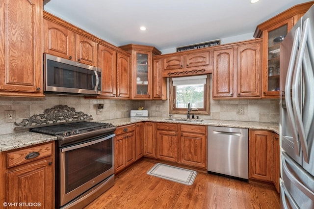 kitchen featuring appliances with stainless steel finishes, light stone countertops, sink, and light wood-type flooring