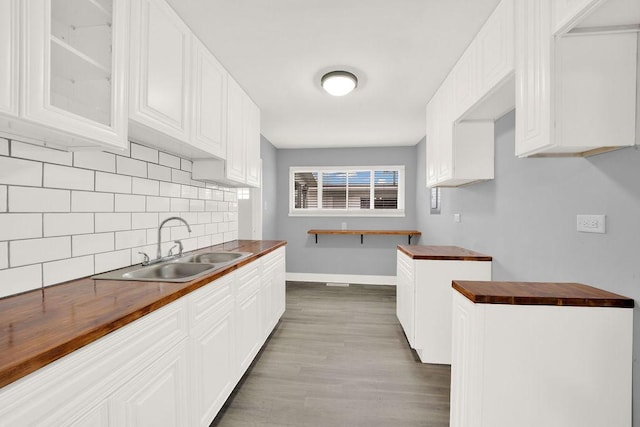 kitchen with backsplash, white cabinets, sink, butcher block countertops, and light hardwood / wood-style floors