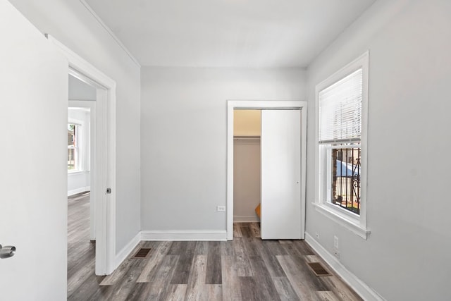 unfurnished bedroom featuring a walk in closet, a closet, and dark hardwood / wood-style flooring