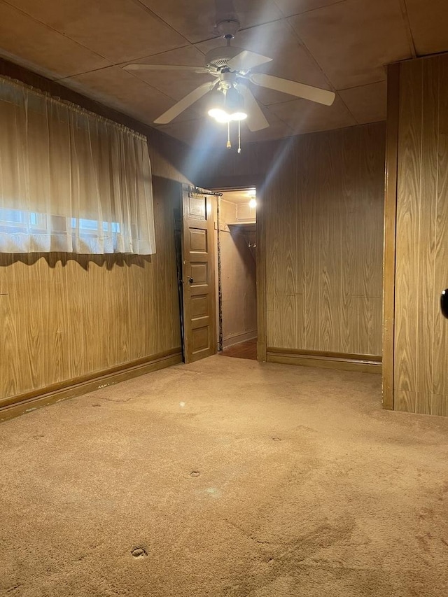 basement featuring carpet floors, ceiling fan, and wood walls