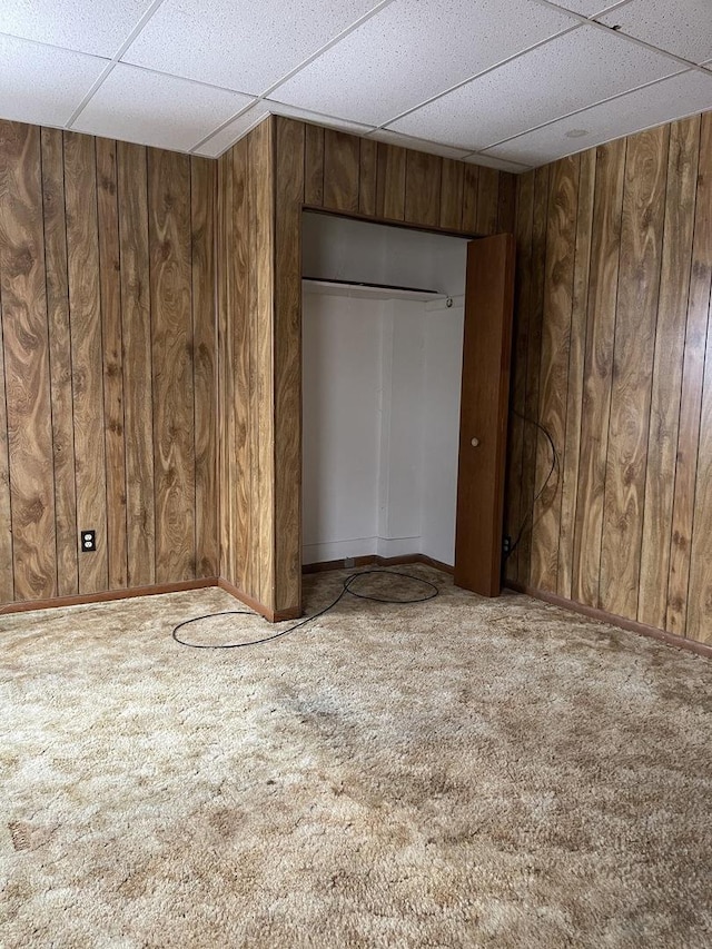 unfurnished bedroom featuring a paneled ceiling, wood walls, a closet, and carpet floors