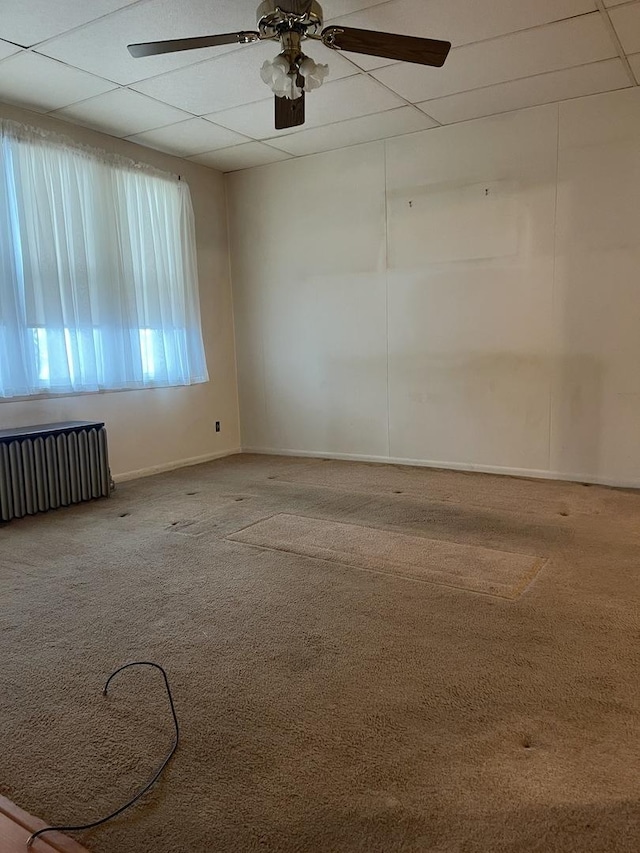 carpeted empty room featuring a paneled ceiling, radiator, and ceiling fan