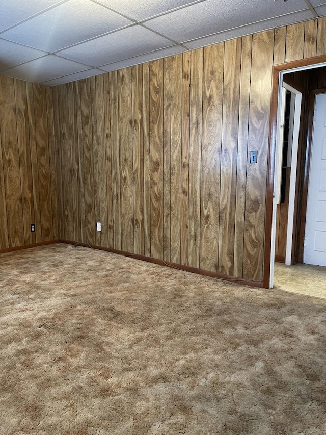 carpeted spare room with a paneled ceiling and wood walls