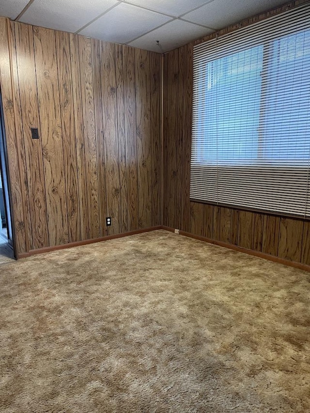 carpeted empty room featuring wood walls and a drop ceiling