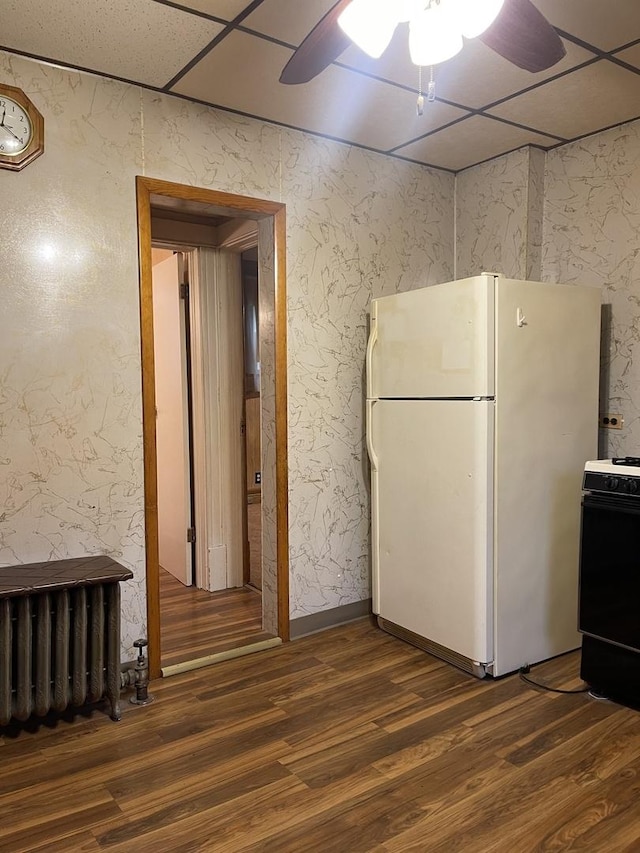 kitchen featuring a paneled ceiling, dark wood-type flooring, white refrigerator, black range with electric cooktop, and radiator heating unit