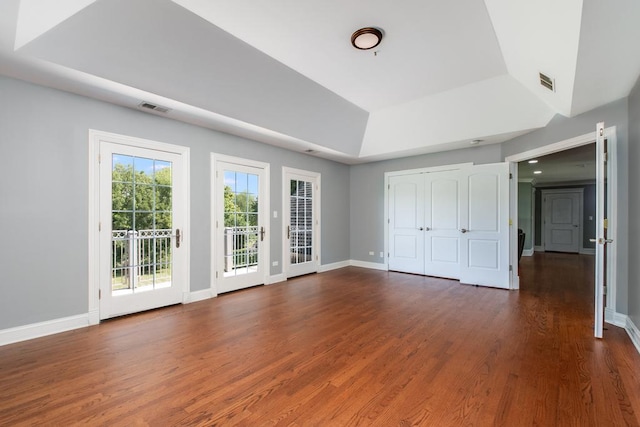 unfurnished bedroom featuring access to exterior, dark hardwood / wood-style flooring, and a raised ceiling